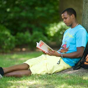 a student reading a book while seated outside under a tree