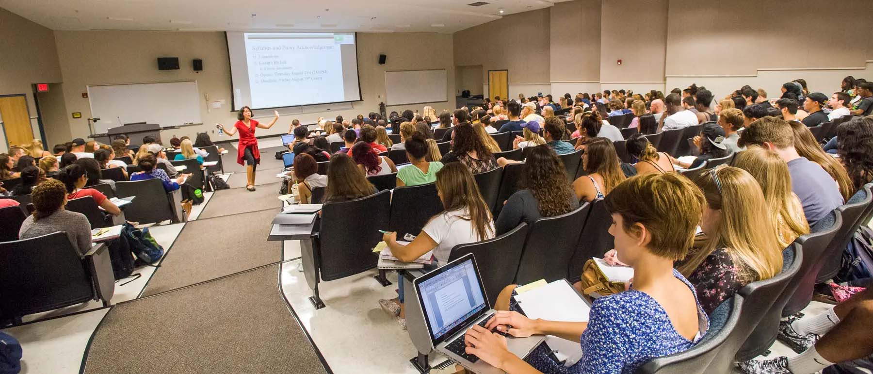 professor teaching a large class full of students who are taking notes