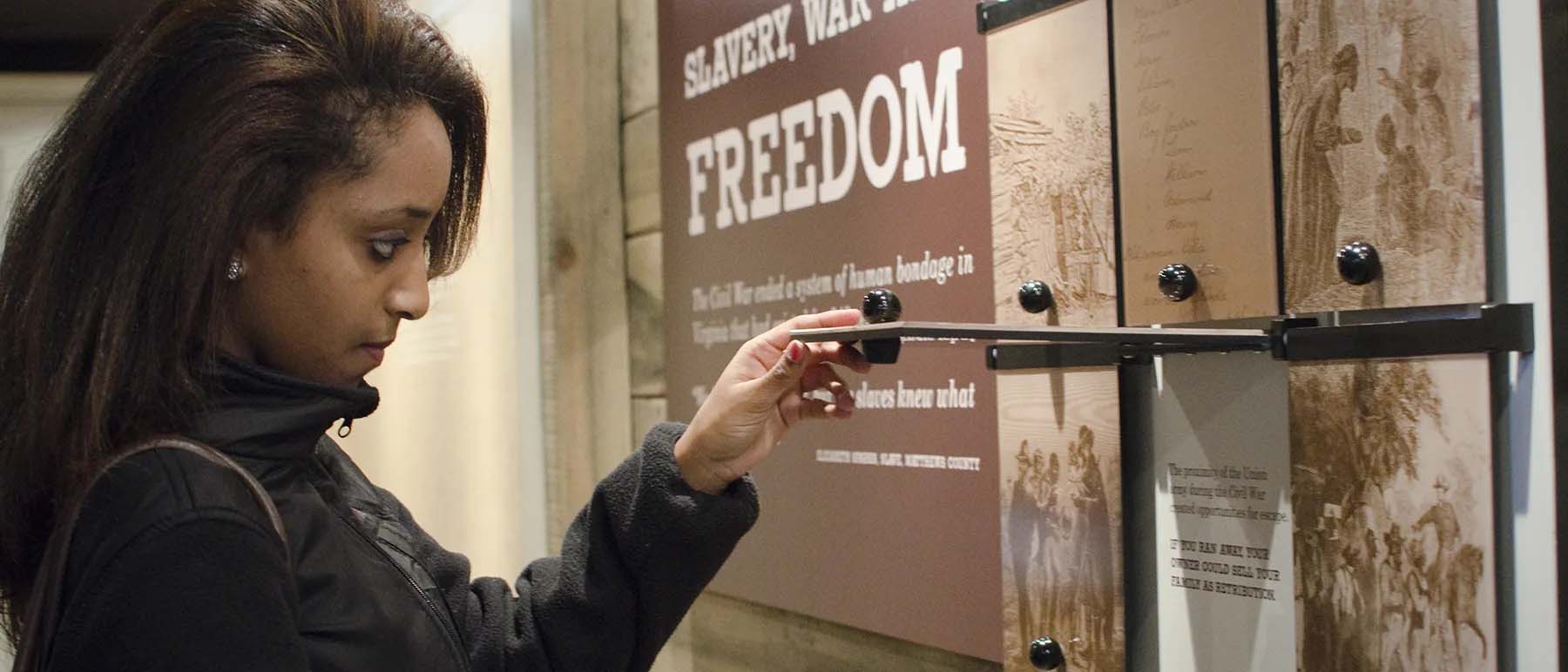 a museum visitor inspects an informational panel in an exhibit titled 'slavery, war, and freedom'
