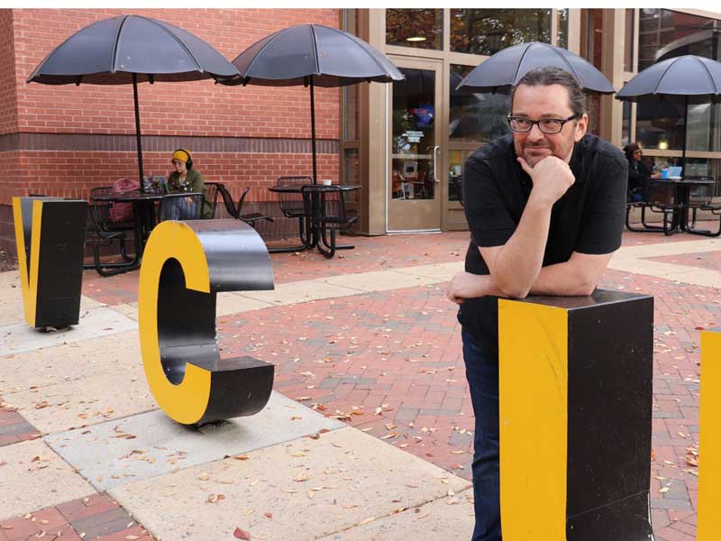 greg smithers posing near statuettes of the letters v.c.u. on the v.c.u. campus